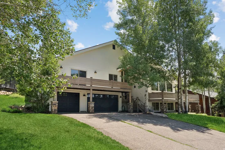 Contemporary exterior with a multi-level design, attached two-car garage, upper-level balcony with wood railing, and mature trees on a sloped lot