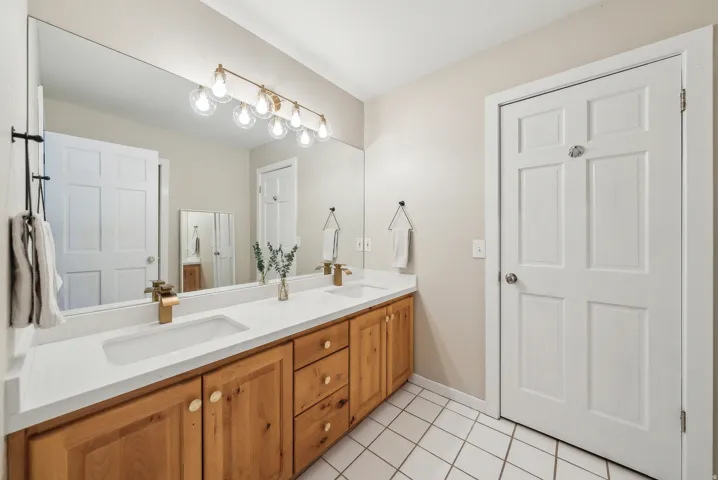 Dual vanity with integrated sinks, wood-finish cabinetry, a full-width mirror, and a multi-bulb light fixture