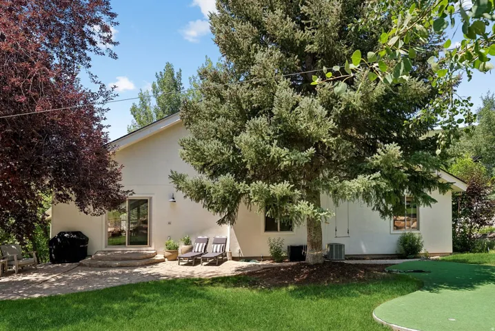 Rear exterior with a stone patio, sliding glass door access, an expansive lawn, mature foliage, and a putting green