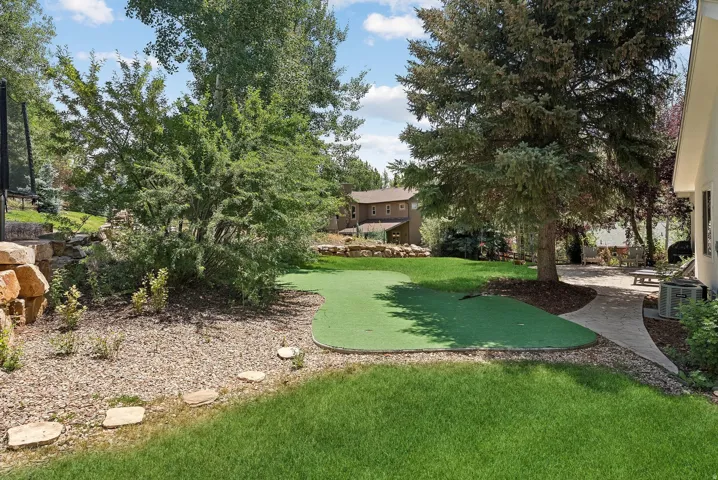 Expansive backyard with a putting green, mature trees, a natural stone retaining wall, a paved patio, and stepping stones