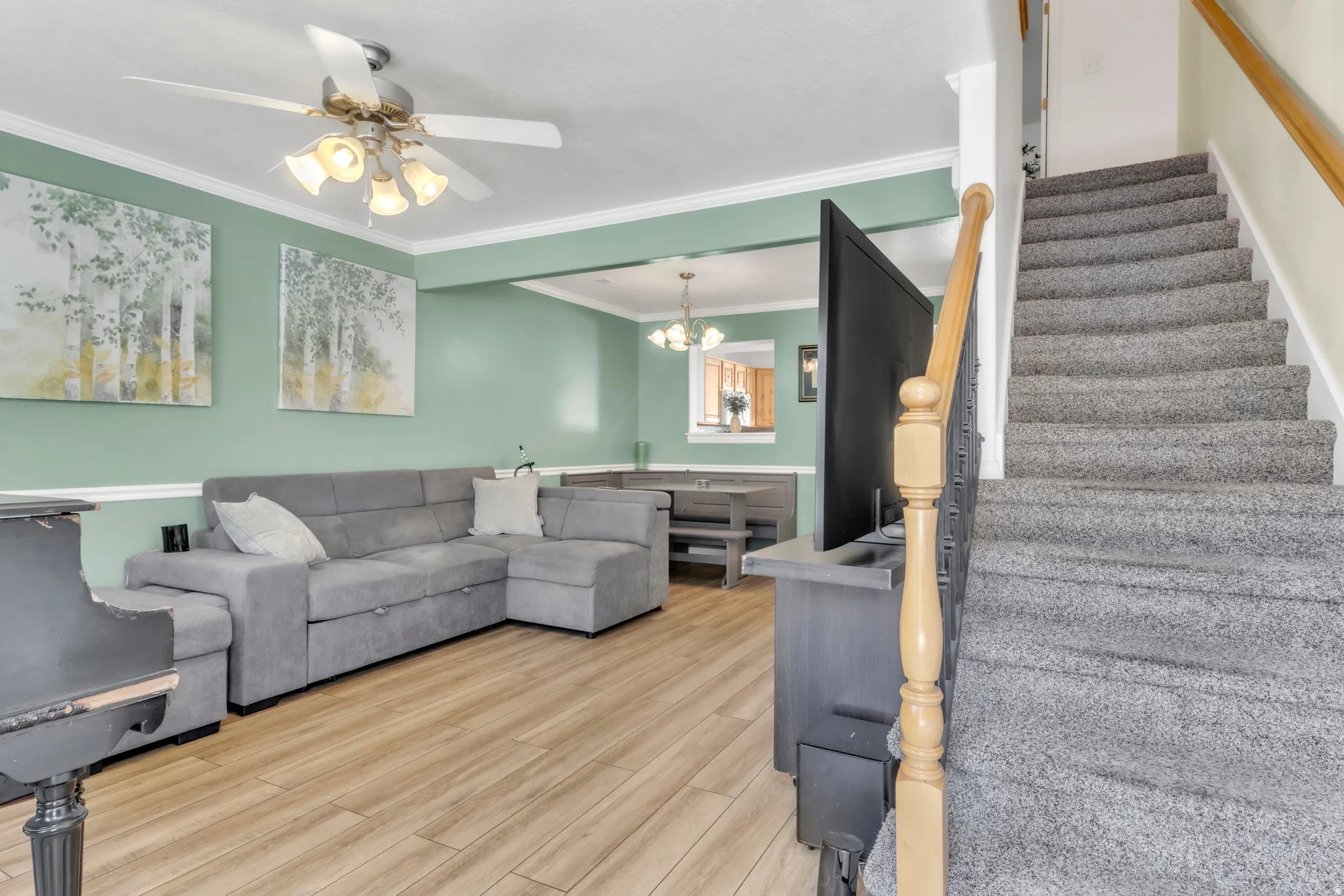 Living area with light wood-type flooring, a chandelier, stairs, crown molding, and a ceiling fan