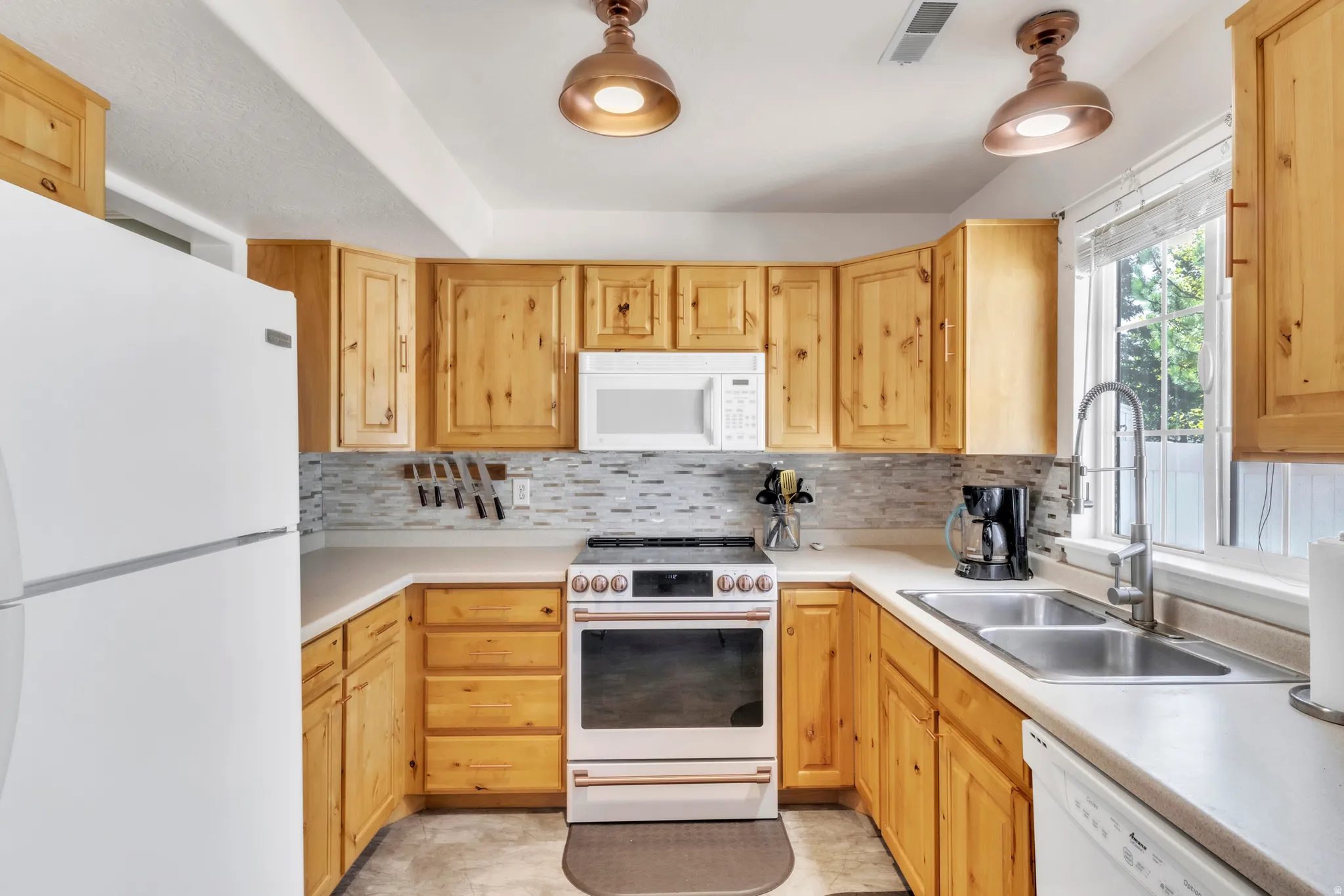 Kitchen featuring white appliances, light countertops, and light brown cabinets