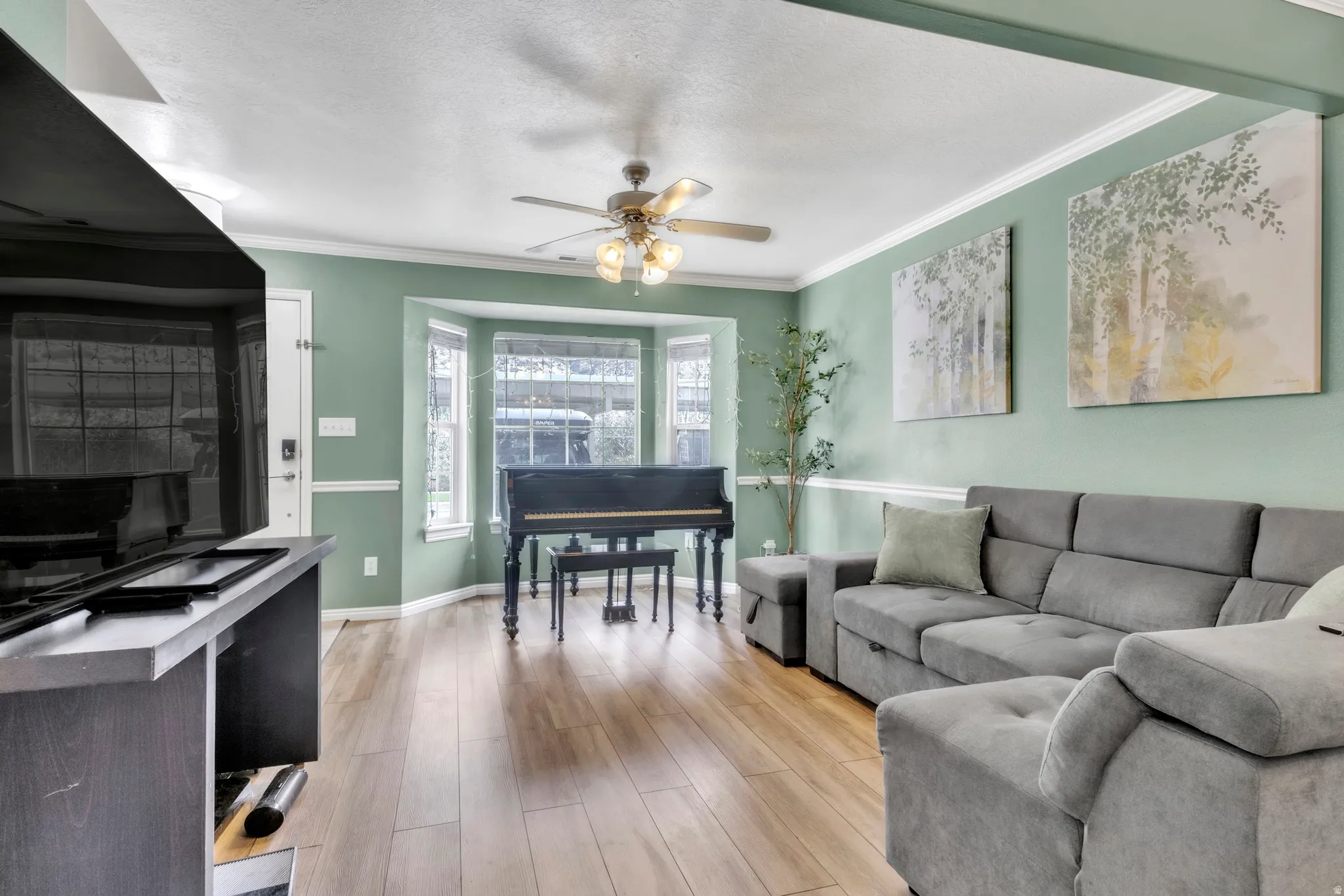 Living area with light wood finished floors, ornamental molding, a ceiling fan, and a textured ceiling