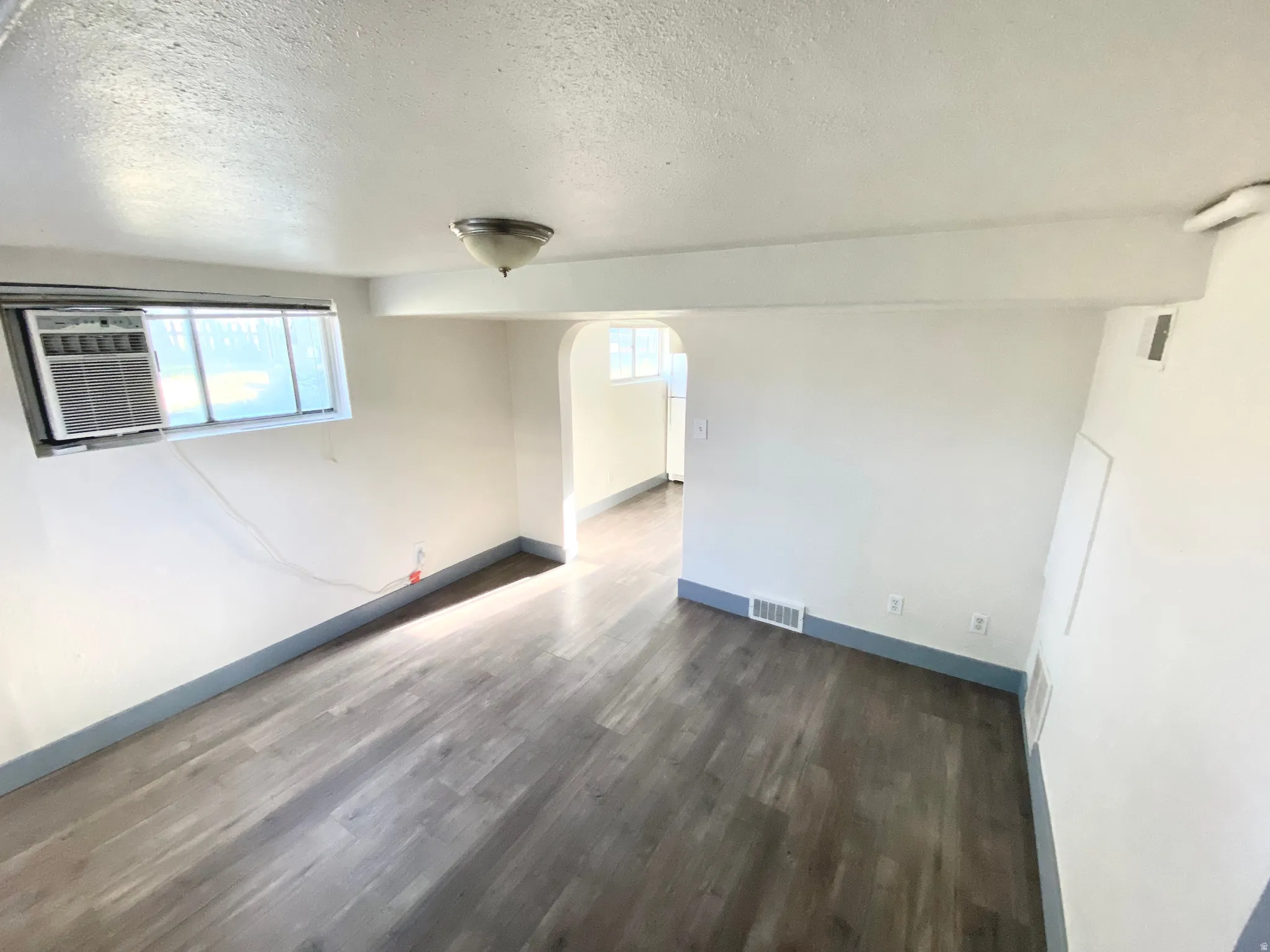 Empty room featuring a textured ceiling, dark wood-type flooring, and arched walkways