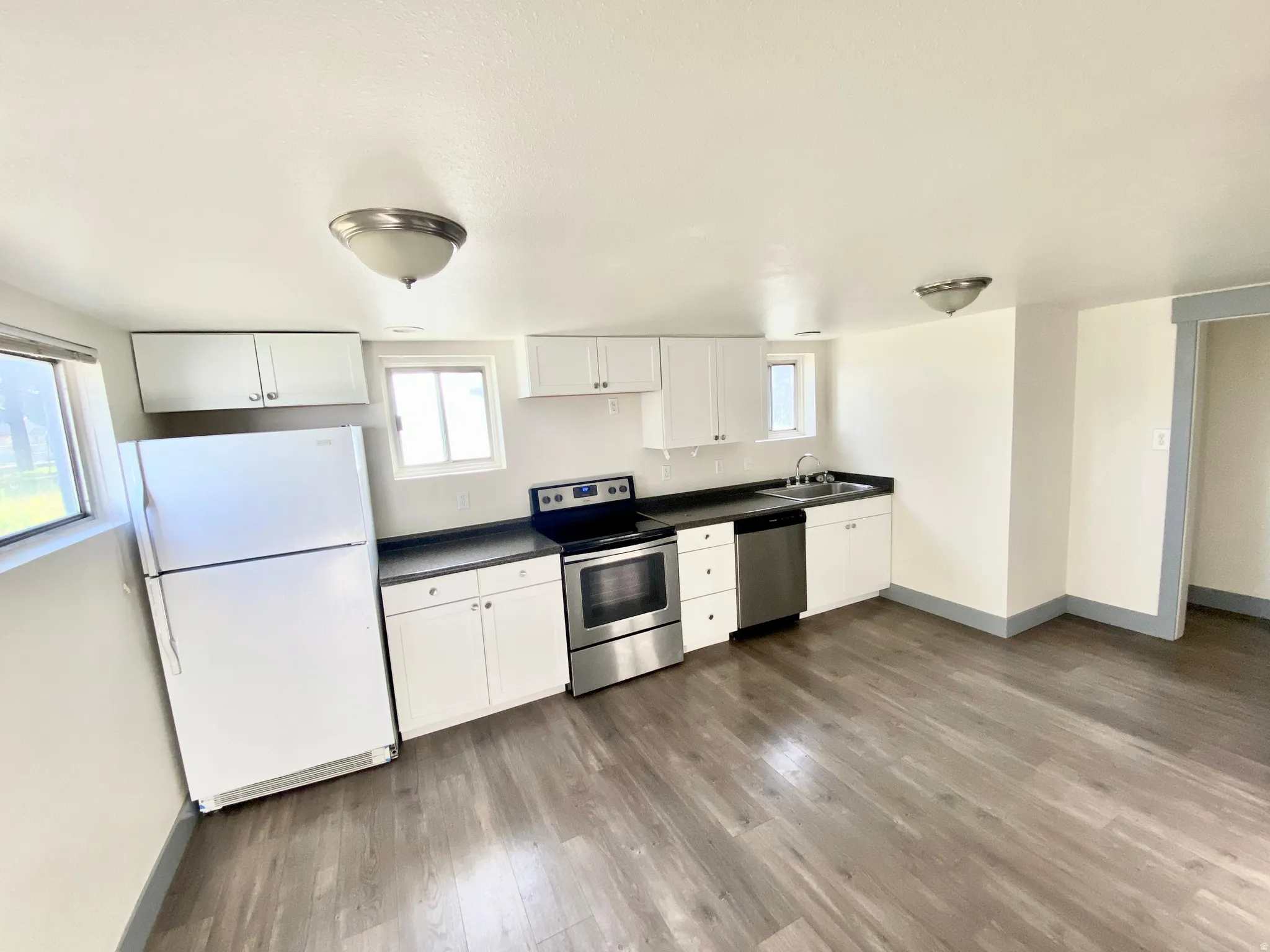 Kitchen with appliances with stainless steel finishes, white cabinets, light wood-style flooring, and dark countertops