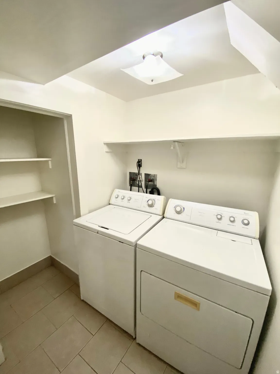 Washroom with independent washer and dryer, a skylight, and light tile patterned flooring