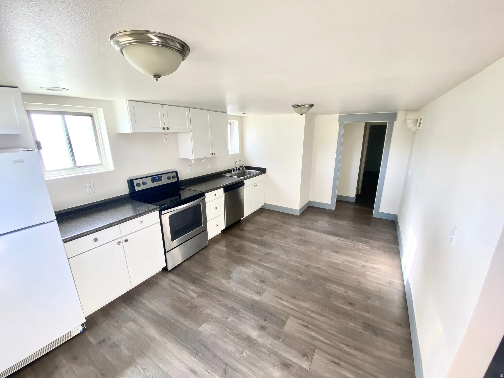 Kitchen featuring white cabinets, stainless steel appliances, dark countertops, and dark wood-type flooring