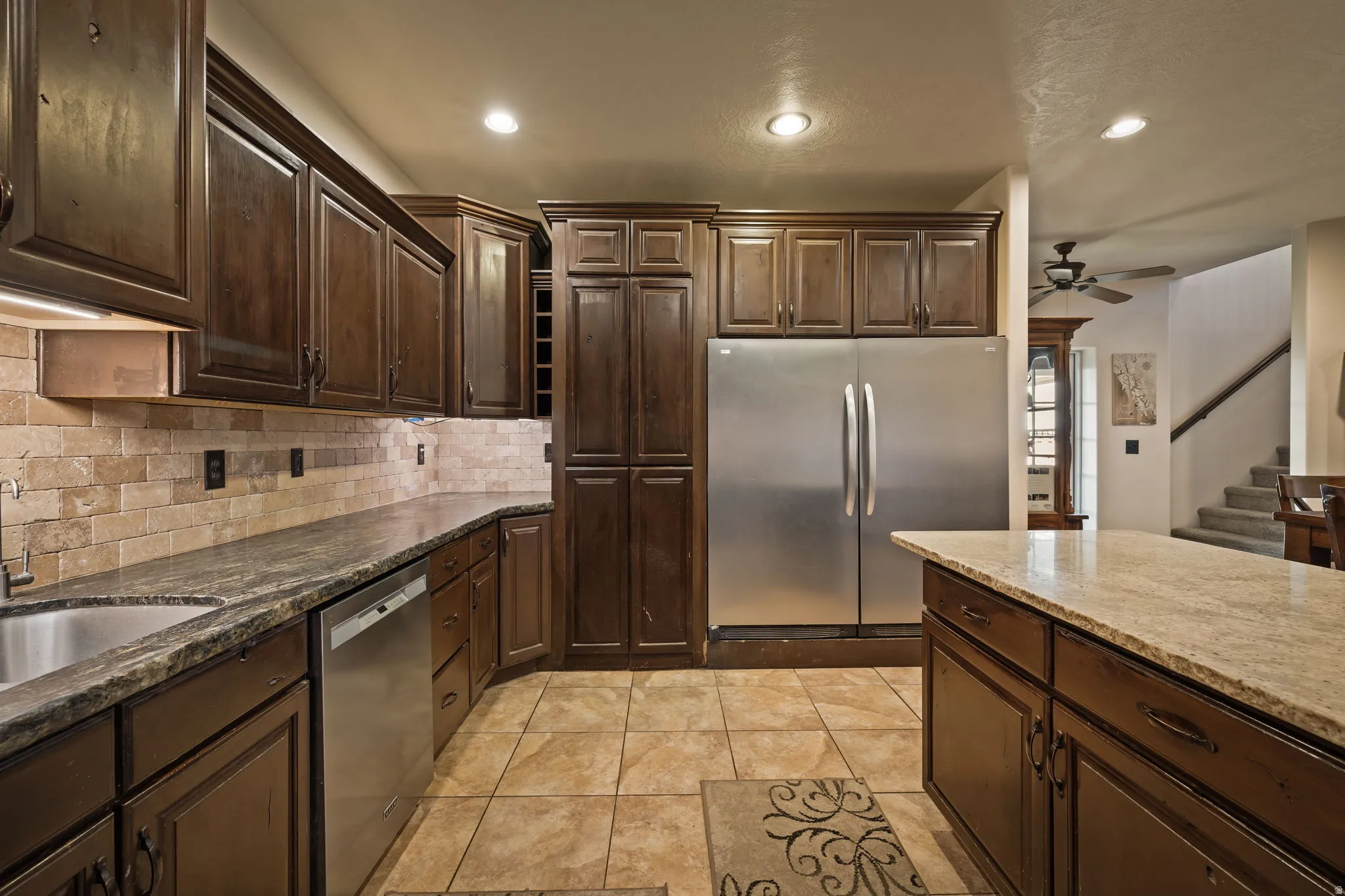 Kitchen with appliances with stainless steel finishes, dark brown cabinets, dark stone countertops, a ceiling fan, and recessed lighting