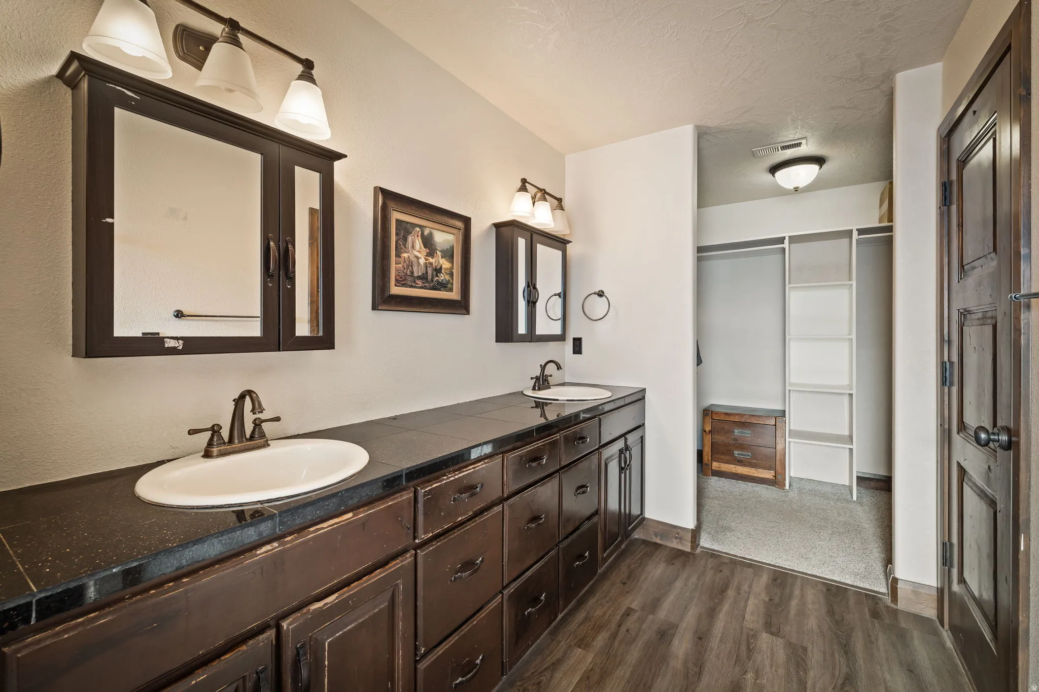 Full bath with double vanity, dark wood-style floors, a walk in closet, and a textured ceiling