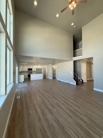 Vaulted ceilings with recessed lighting, wood-finish flooring, a contemporary ceiling fan, and a kitchen featuring white cabinetry and an island