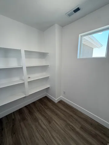 Room featuring built-in shelving, wood-finish flooring, a single window, and a white color palette