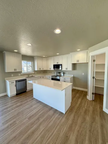 Kitchen featuring wood-finish flooring, white cabinetry, a central island with a solid surface countertop, stainless steel appliances, and recessed lighting