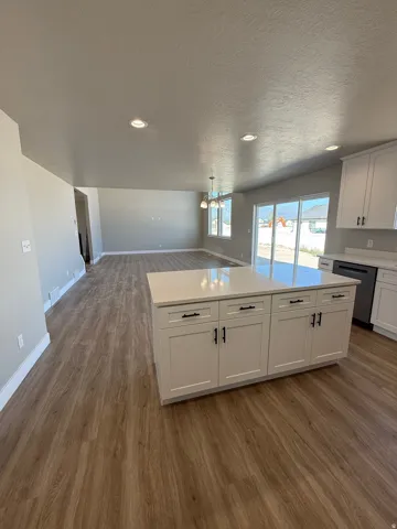 Open-concept living space featuring wood-finish flooring, recessed lighting, and a kitchen island with stone countertops