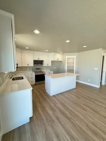 Kitchen featuring white cabinetry, light-toned countertops, stainless steel appliances, a center island, and wood-finish flooring