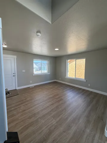 Spacious room with wood-finish flooring, two large windows, white trim, and recessed lighting
