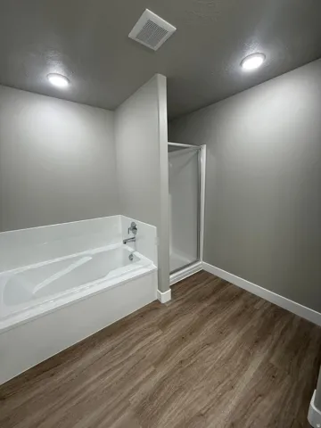 Bathroom featuring a built-in bathtub, separate shower enclosure, wood-finish flooring, and recessed ceiling lighting