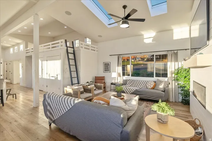 Living room featuring a high ceiling, hardwood / wood-style floors, ceiling fan, recessed lighting, and a skylight