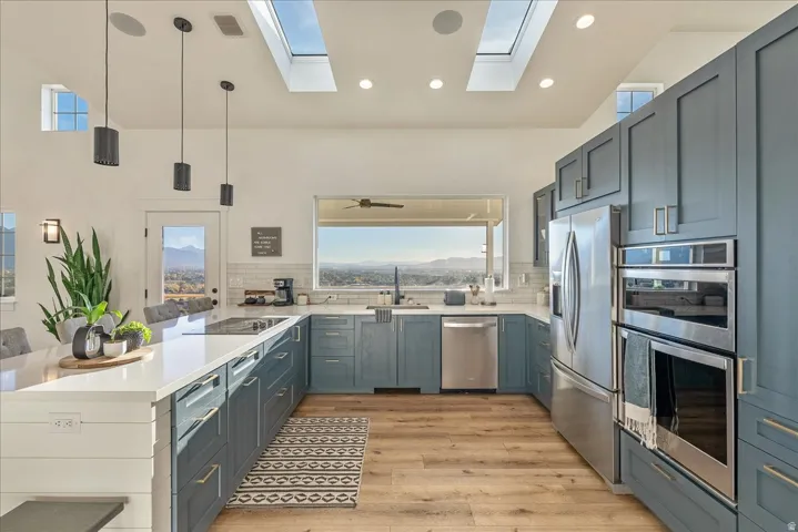Kitchen with decorative light fixtures, stainless steel appliances, a peninsula, light wood-type flooring, and light stone countertops