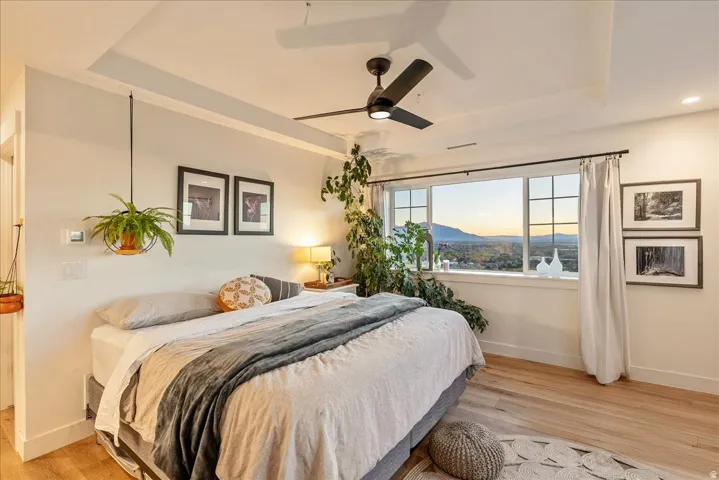 Bedroom with a tray ceiling, light wood finished floors, and ceiling fan