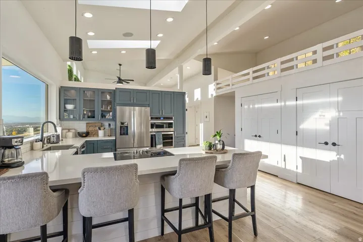 Kitchen with a peninsula, decorative light fixtures, stainless steel appliances, glass insert cabinets, and light wood-style floors
