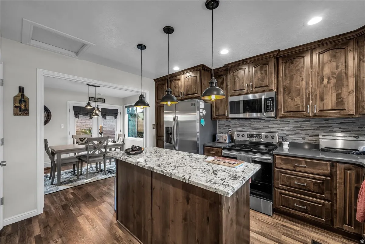 Kitchen with dark brown cabinetry, stainless steel appliances, a kitchen island, decorative light fixtures, and decorative backsplash