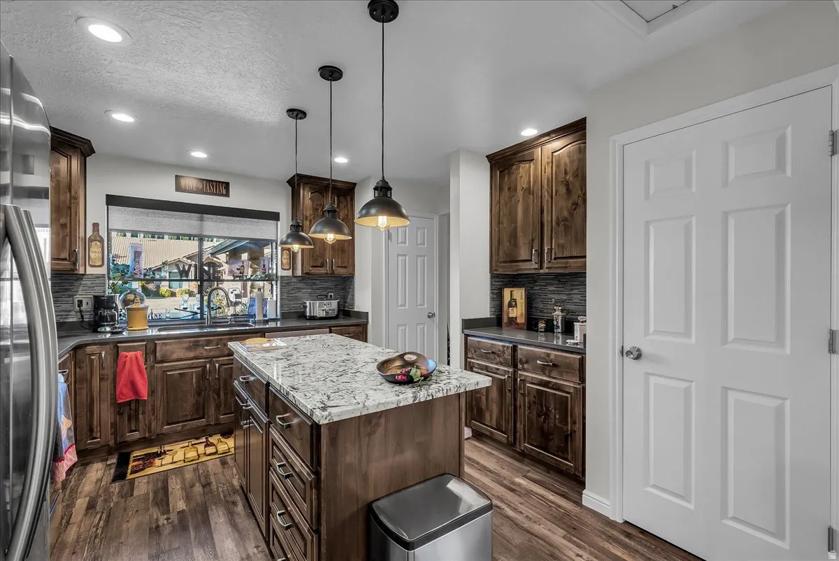 Kitchen featuring dark brown cabinetry, hanging light fixtures, stainless steel refrigerator, a textured ceiling, and dark wood-style floors