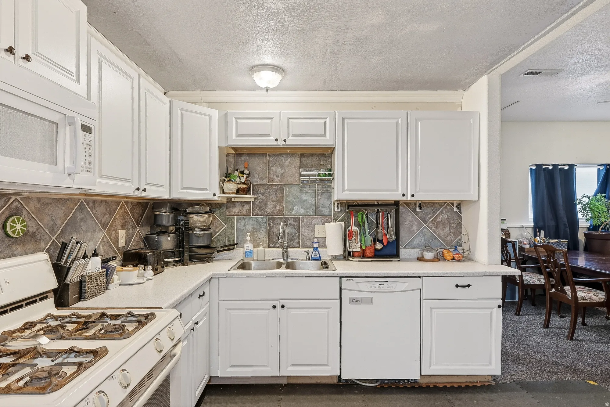 Kitchen with white appliances, white cabinets, light countertops, a textured ceiling, and decorative backsplash