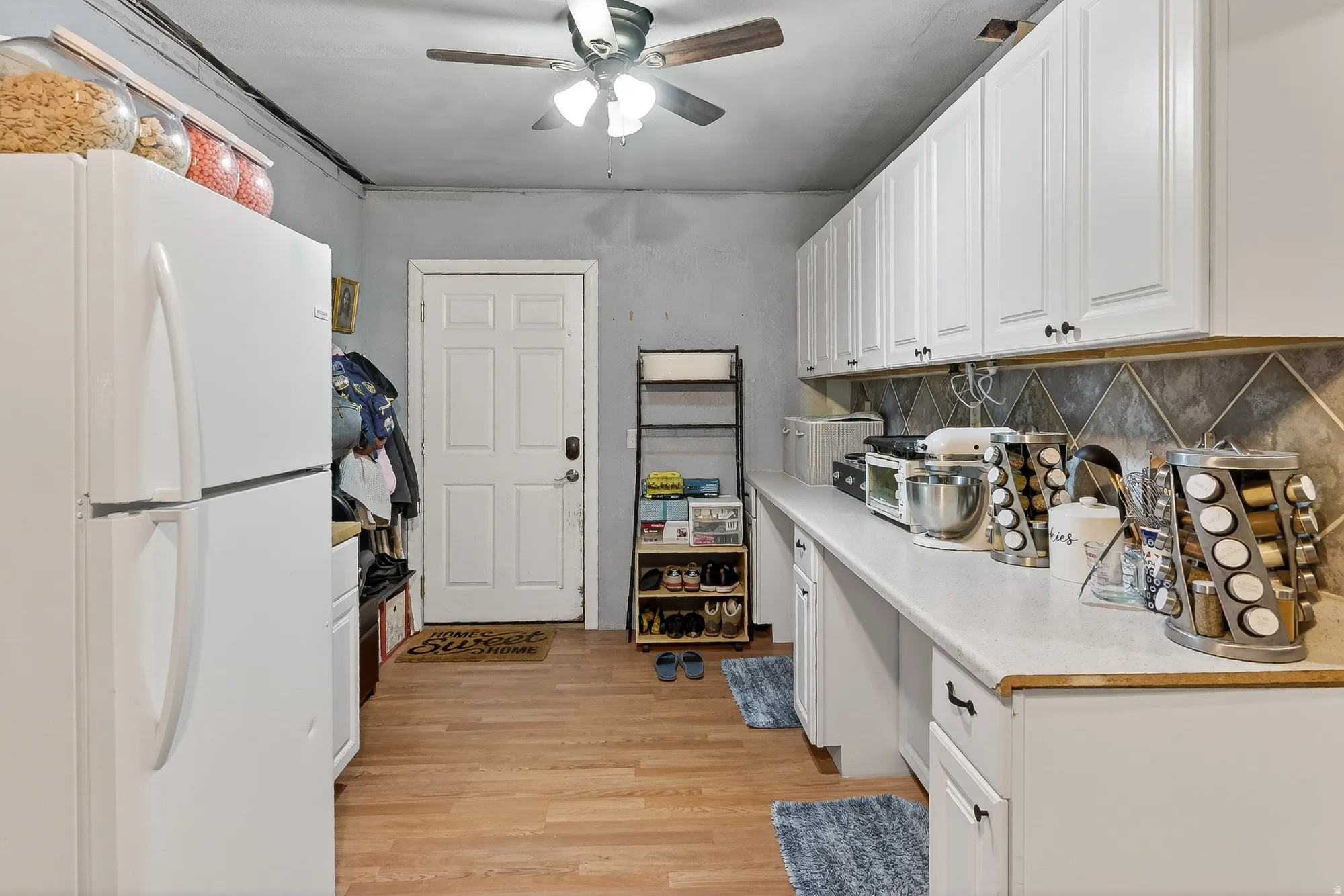 Kitchen with freestanding refrigerator, light countertops, white cabinets, light wood-style floors, and backsplash