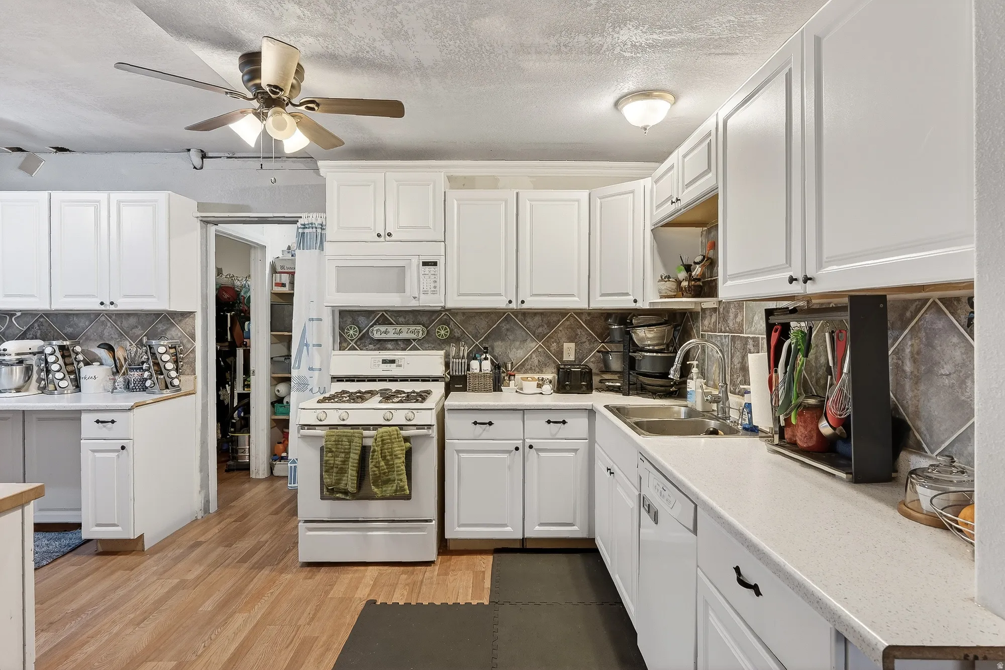 Kitchen with light countertops, white appliances, white cabinets, light wood-type flooring, and a textured ceiling