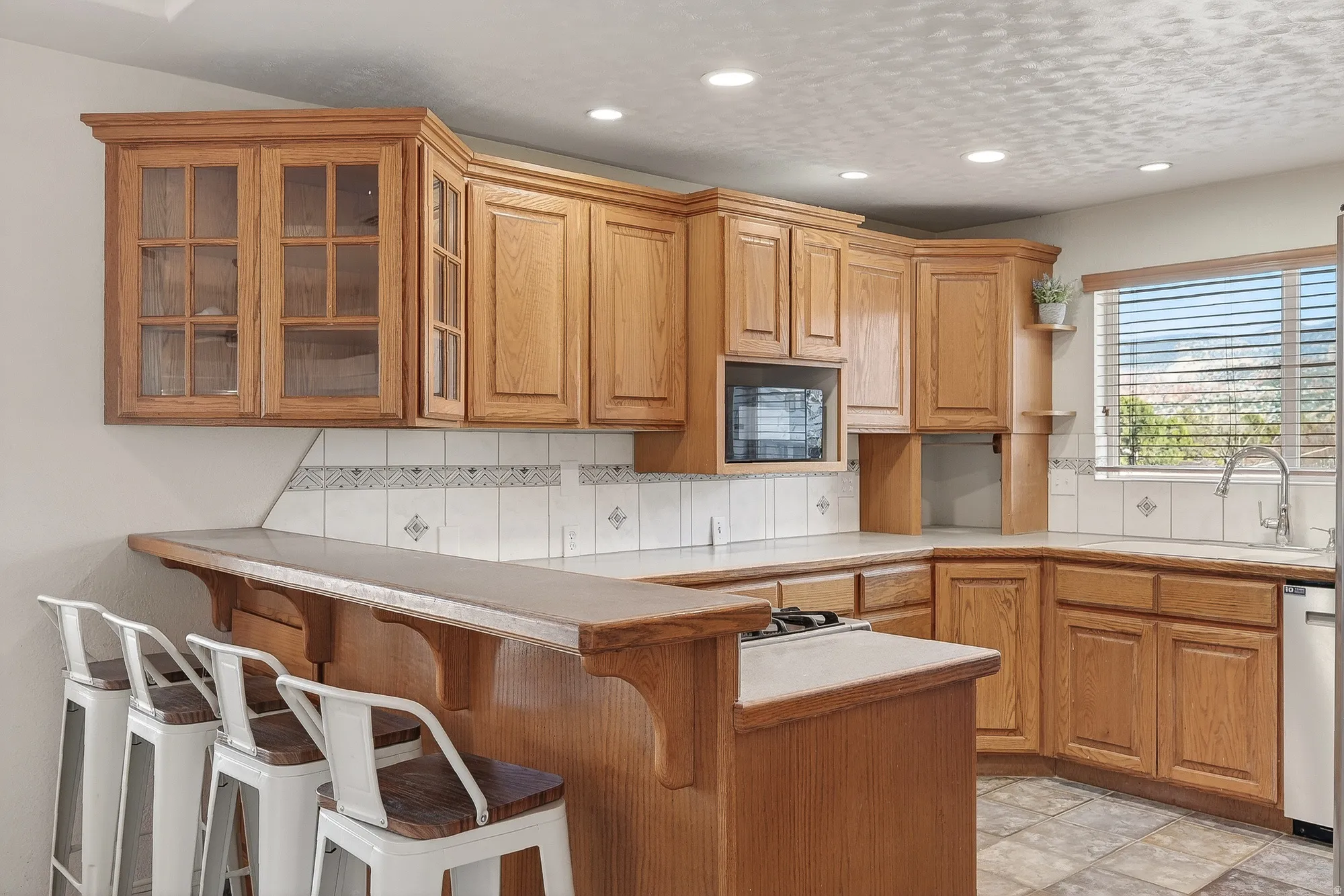 Kitchen featuring a breakfast bar area, backsplash, glass insert cabinets, light countertops, and a peninsula