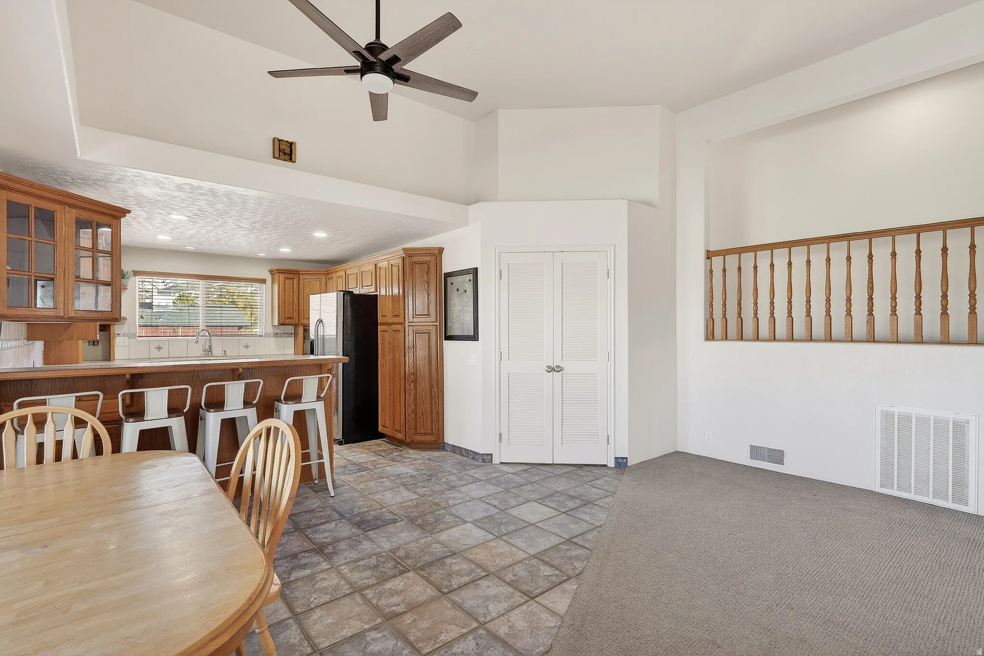 Kitchen featuring glass insert cabinets, brown cabinets, a breakfast bar, light carpet, and stainless steel fridge