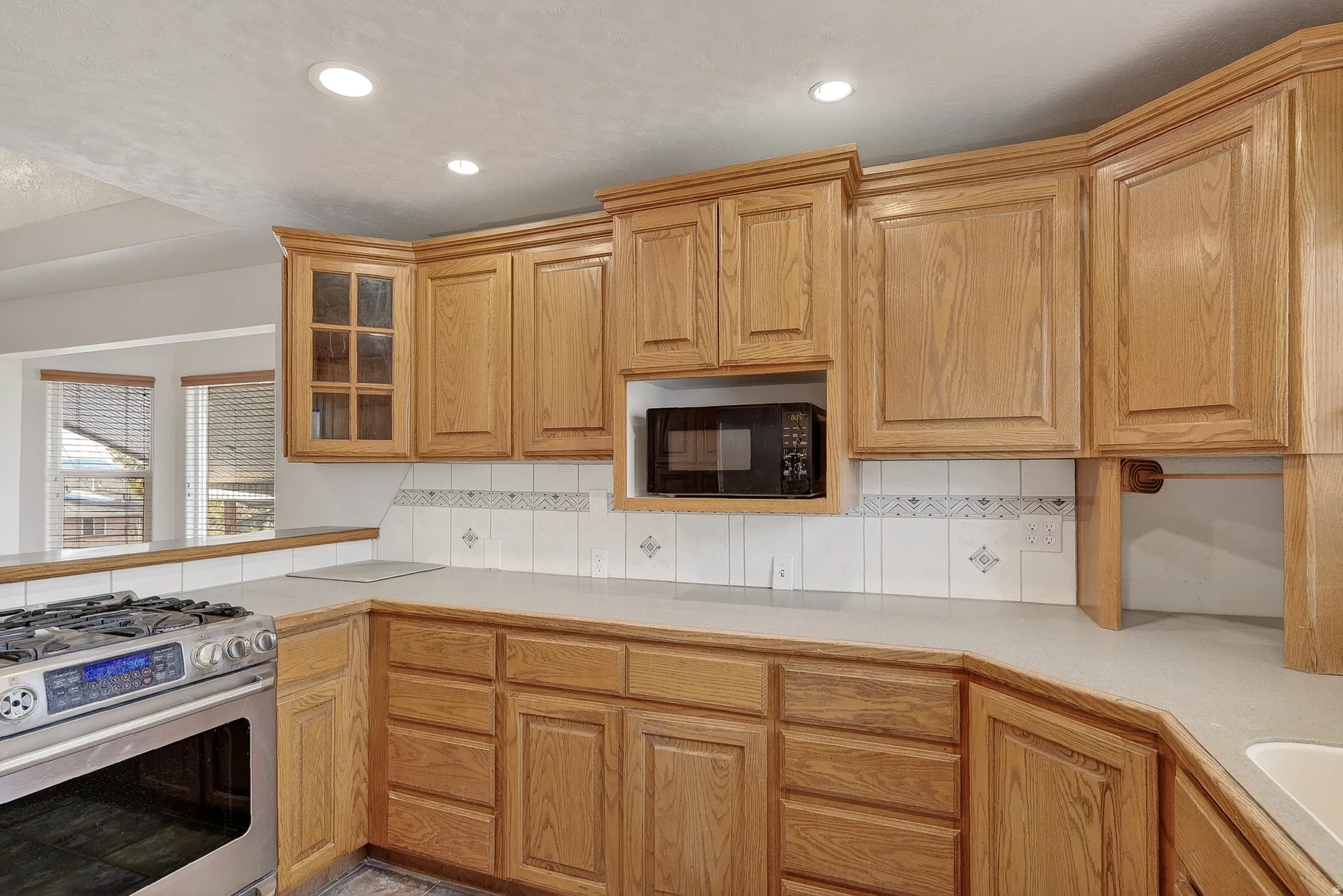 Kitchen with gas range, tasteful backsplash, light countertops, glass insert cabinets, and black microwave