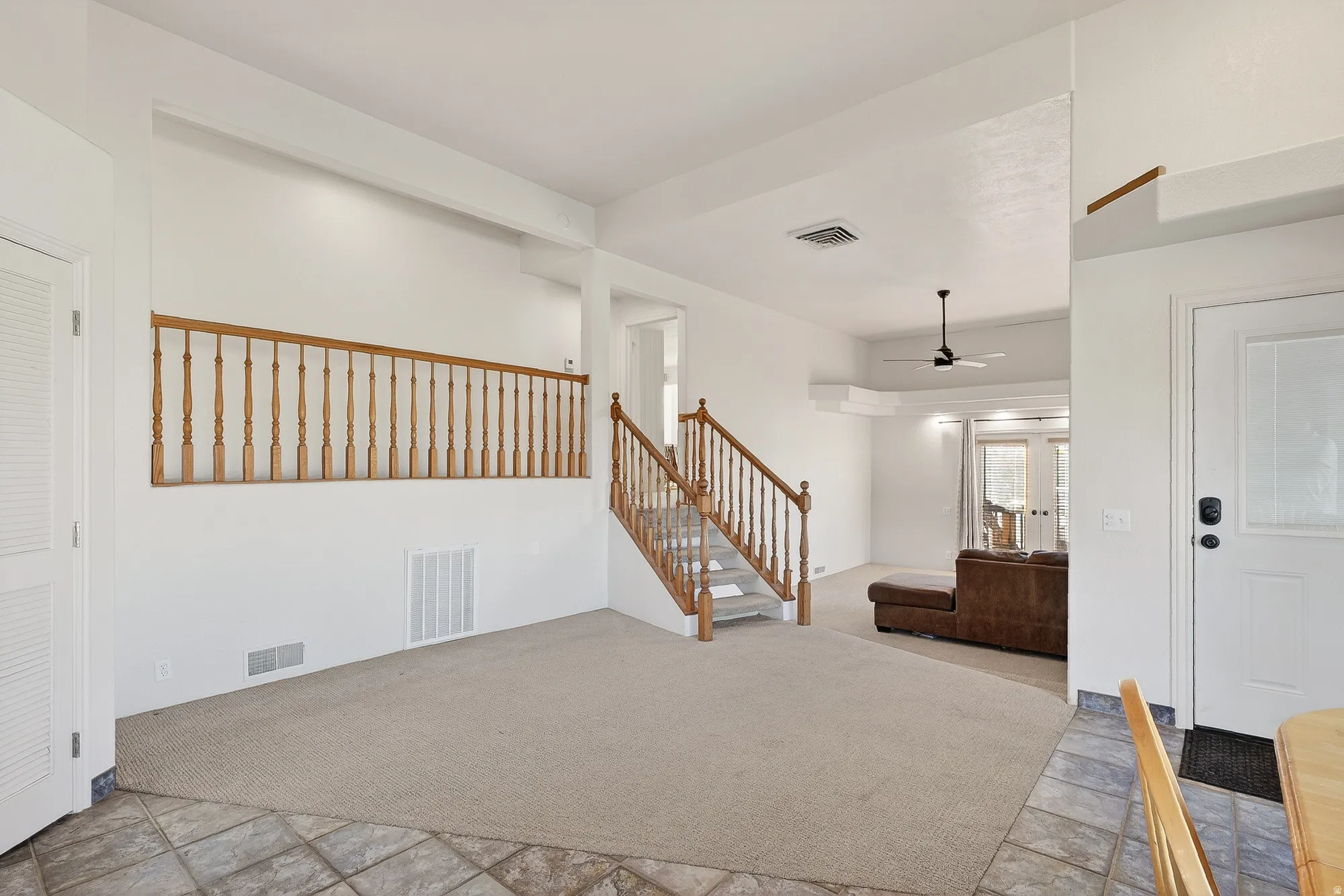 Foyer with light colored carpet, stairway, a ceiling fan, and light stone finish flooring