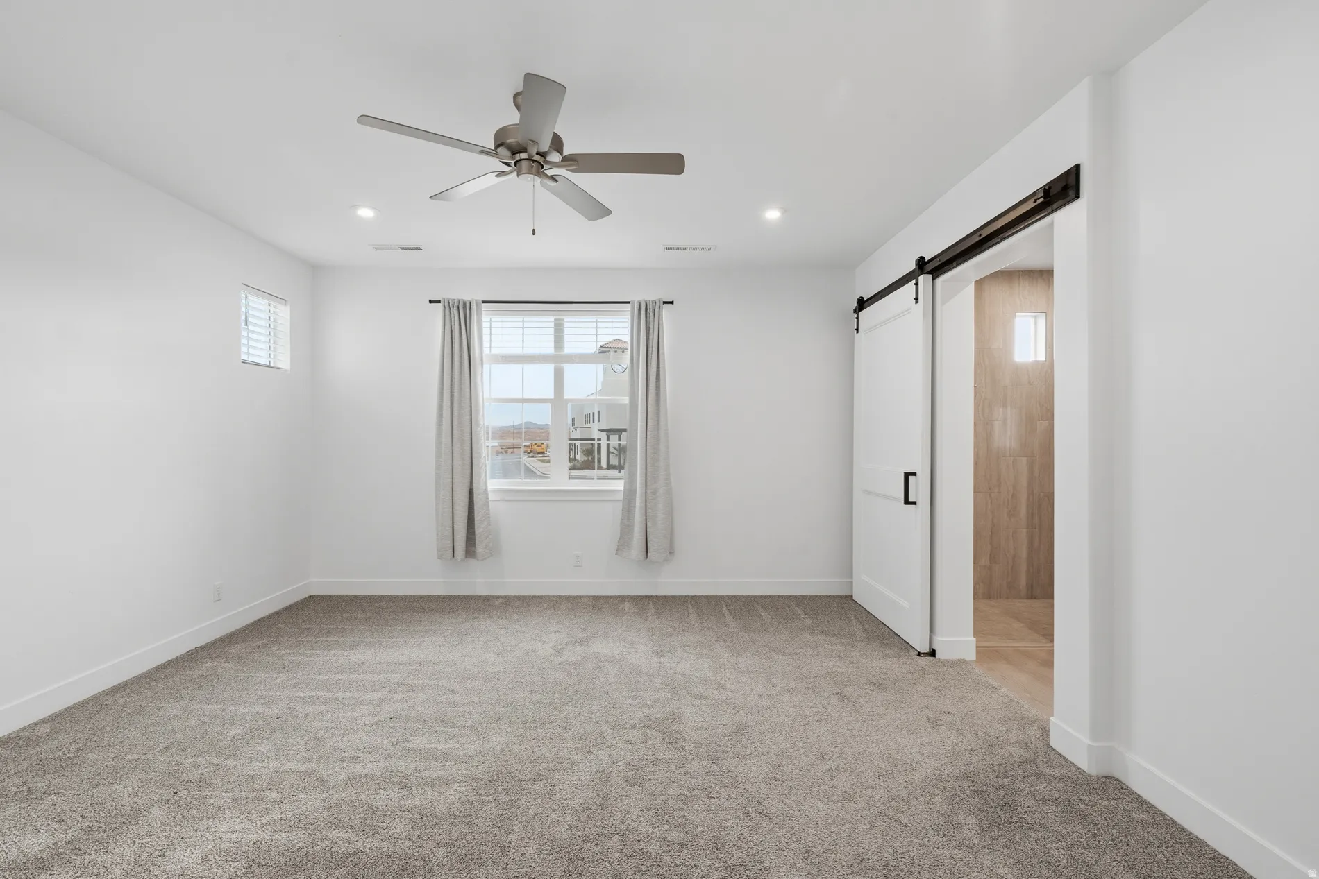 Empty room with light carpet, a barn door, ceiling fan, and recessed lighting