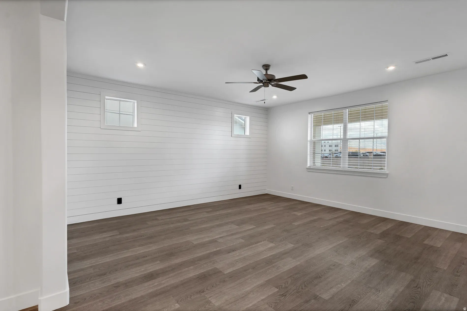 Wood-finish flooring, recessed lighting, ceiling fan, multiple windows, and a shiplap accent wall