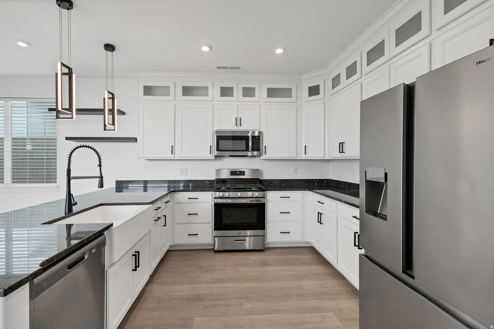 White shaker cabinetry with black hardware, stainless steel appliances, dark stone countertops, wood-finish flooring, and a farmhouse sink