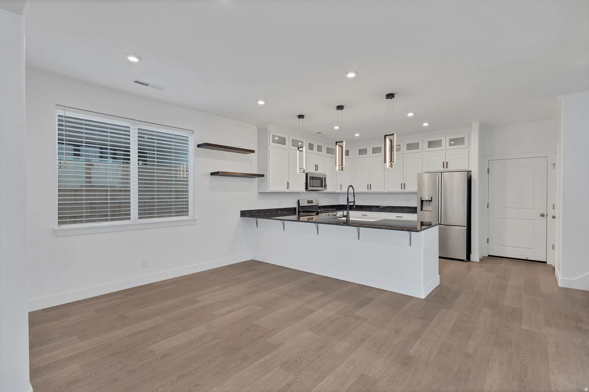 Open-concept kitchen featuring white cabinetry, dark stone countertops, stainless steel appliances, and a breakfast bar