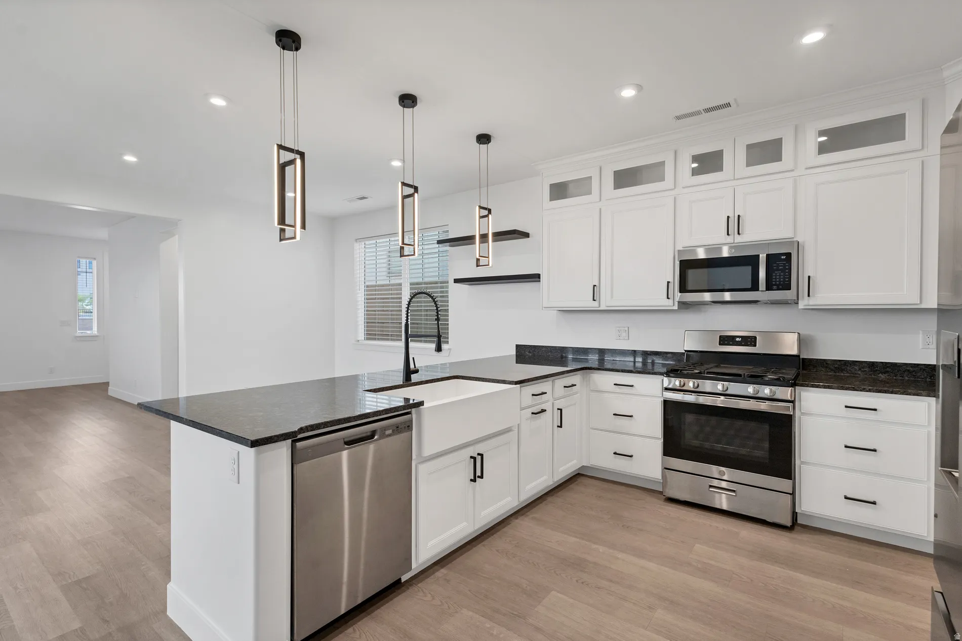 Modern kitchen featuring white cabinetry, dark countertops, stainless steel appliances, and wood-finish flooring