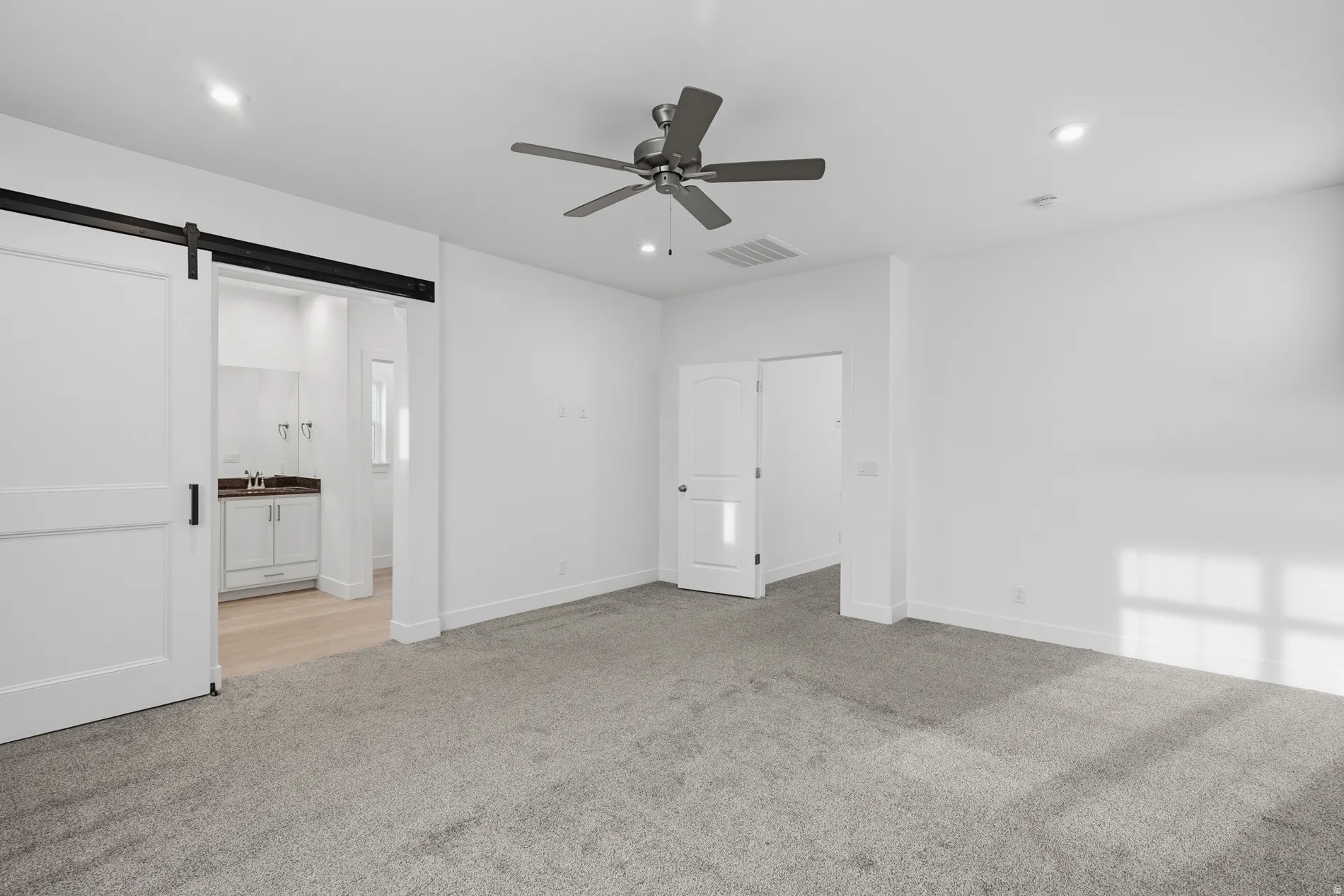 Unfurnished bedroom featuring a barn door, light colored carpet, recessed lighting, a ceiling fan, and ensuite bathroom