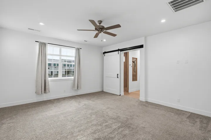 Unfurnished bedroom featuring a barn door, light carpet, ceiling fan, recessed lighting, and connected bathroom