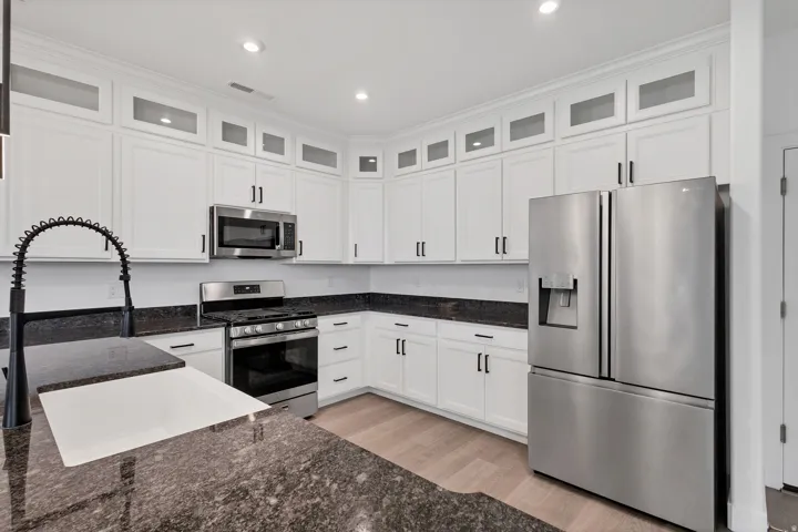 White cabinetry with glass-front uppers, stainless steel appliances, dark stone countertops, wood-finish flooring, and a gooseneck faucet