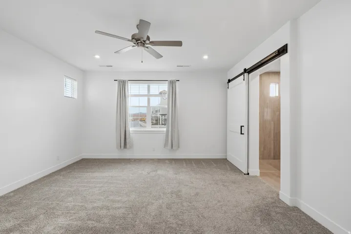 Empty room with light carpet, a barn door, ceiling fan, and recessed lighting