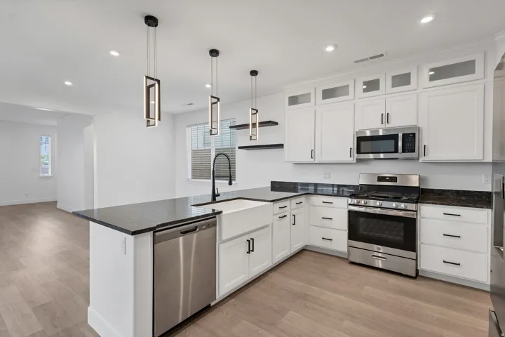 Modern kitchen featuring white cabinetry, dark countertops, stainless steel appliances, and wood-finish flooring