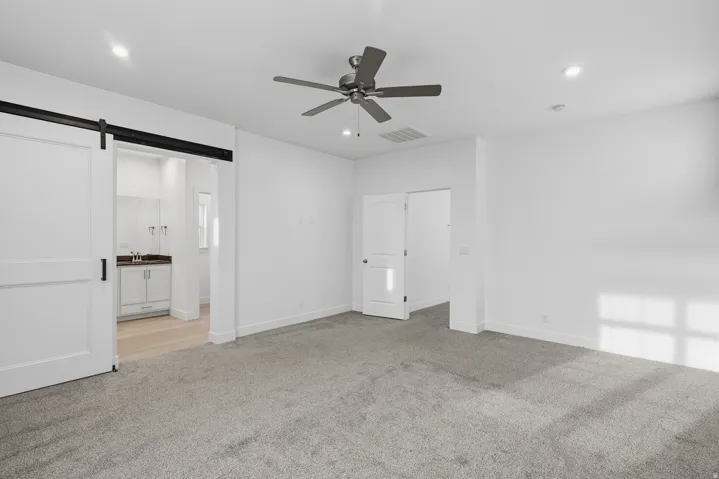 Unfurnished bedroom featuring a barn door, light colored carpet, recessed lighting, a ceiling fan, and ensuite bathroom