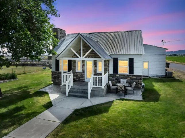 Back of house at dusk with a metal roof, a chimney, stone siding, and a patio