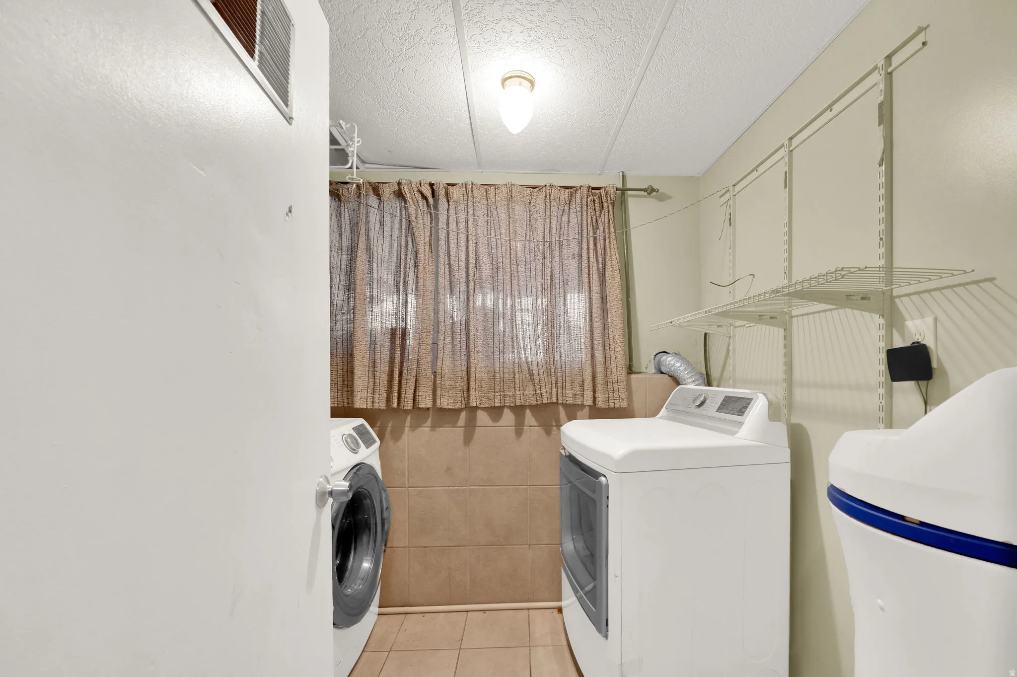 Laundry area featuring a textured ceiling, separate washer and dryer, and light tile patterned flooring