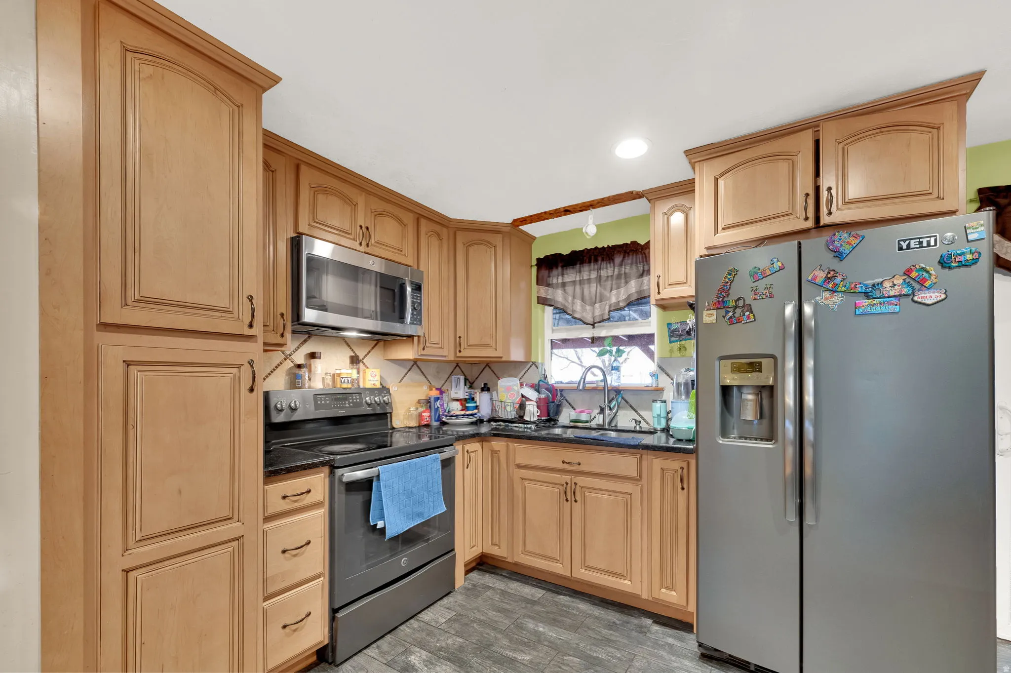 Kitchen with appliances with stainless steel finishes, dark stone countertops, decorative backsplash, light brown cabinets, and light floors