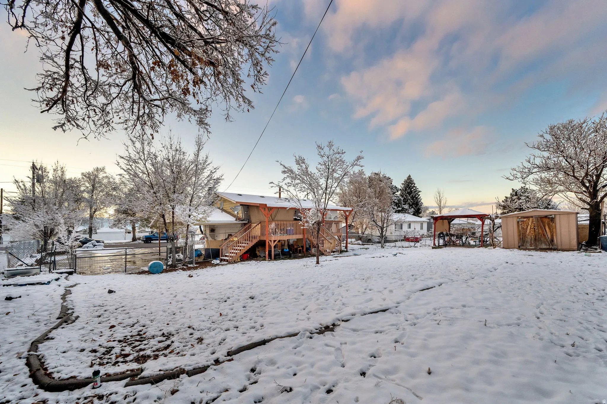 Snow covered property with a wooden deck, stairs, and a storage shed