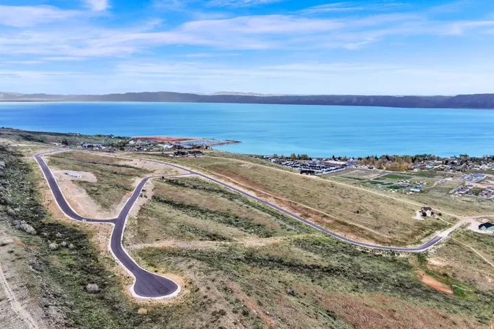 Expansive undeveloped land featuring a cul-de-sac and paved roads, set against a backdrop of a large body of water and distant mountains