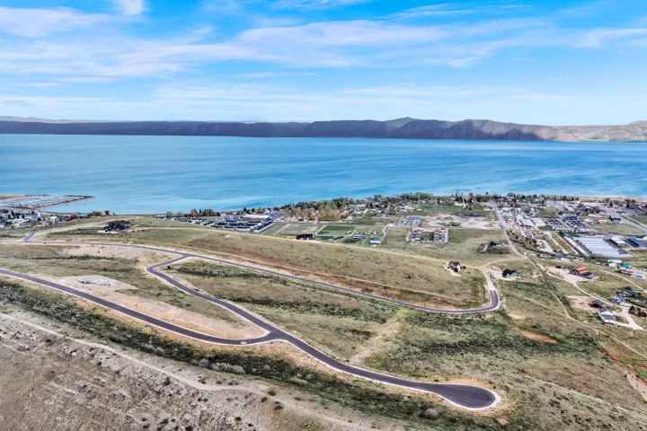 Expansive undeveloped land featuring paved roads and gentle slopes, offering proximity to a large body of water and distant mountainous terrain